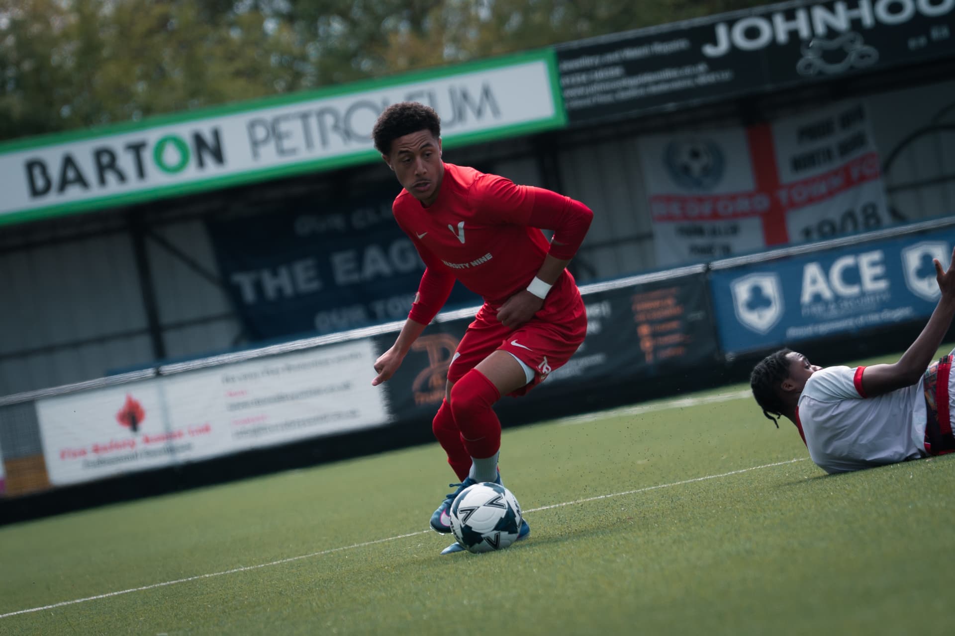 A player driving forward with the ball at a non-league ground